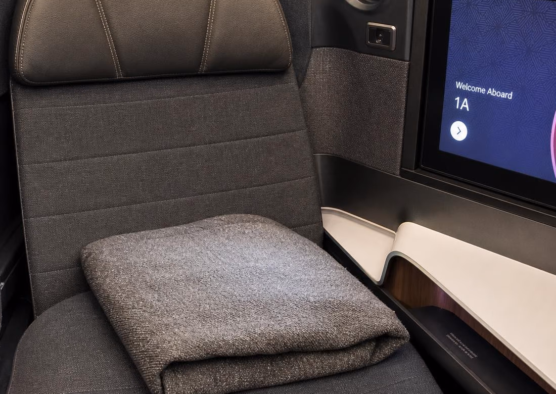 Close view of an airline business seat with a folded blanket and a personal screen