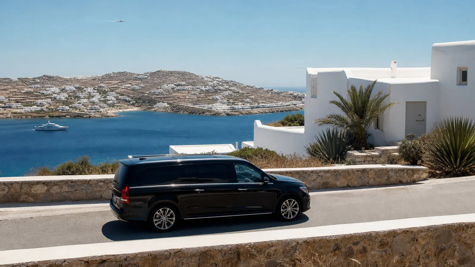 Luxury transfer on a Mykonos coastal road with white Cycladic villas and the Aegean Sea beyond